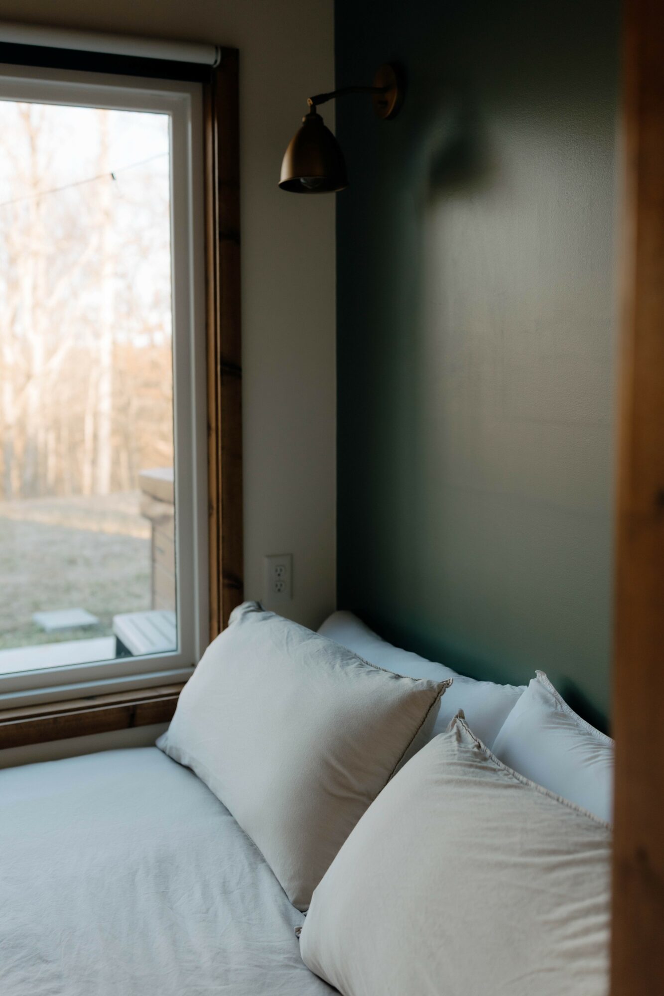Bed with white pillows near a window with a view of trees outside.