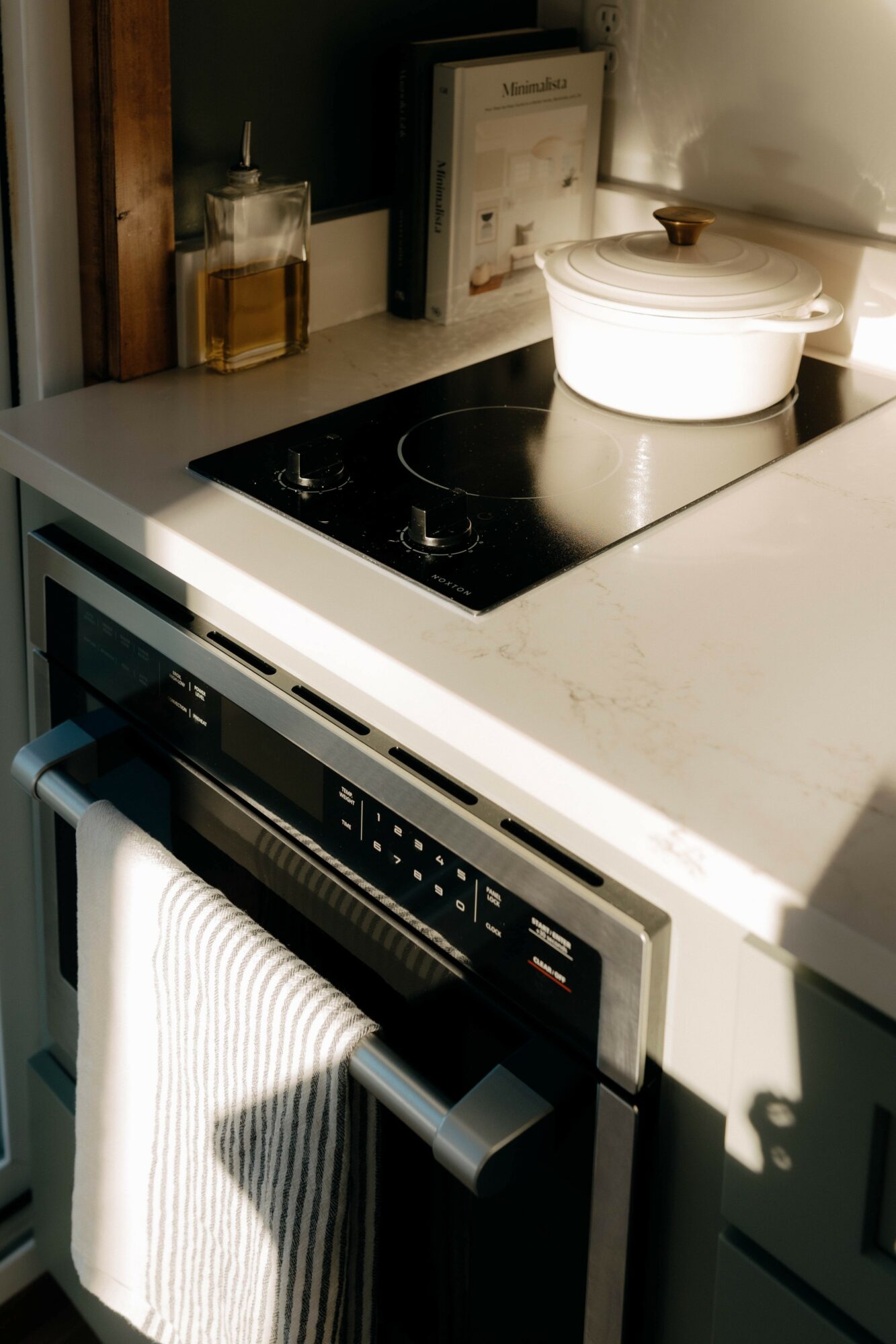 Kitchen countertop with a white pot, glass jar, and framed picture, stove, and oven below with a towel hanging.