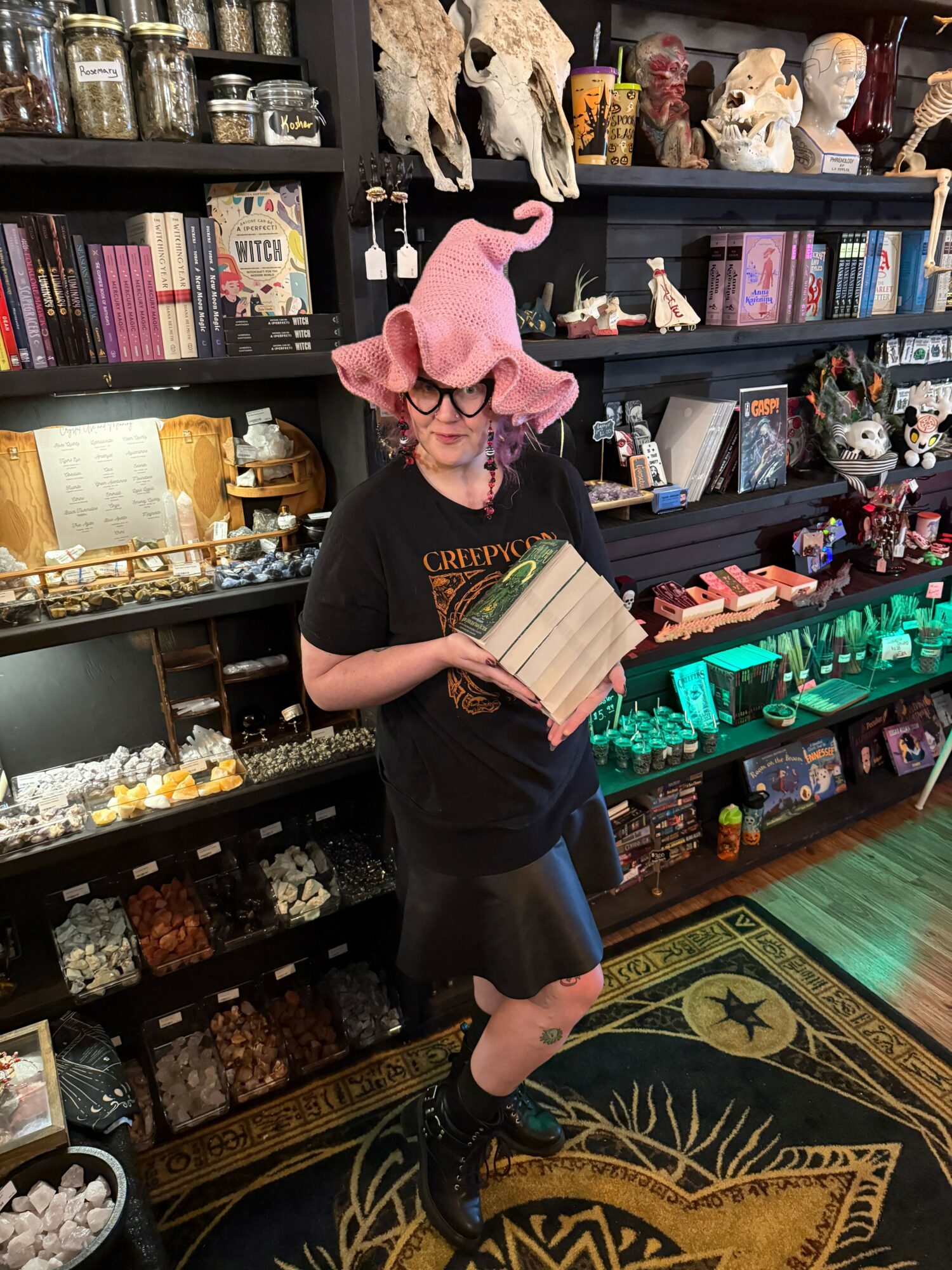 Person wearing a pink animal hat reading a book in a store with shelves of collectibles and books.