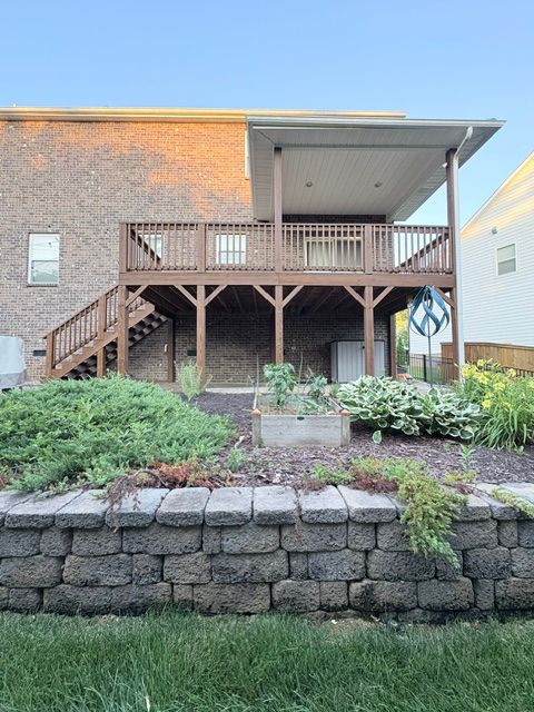 Backyard with wooden deck, stairs, garden plants, and stone border, viewed from the side.