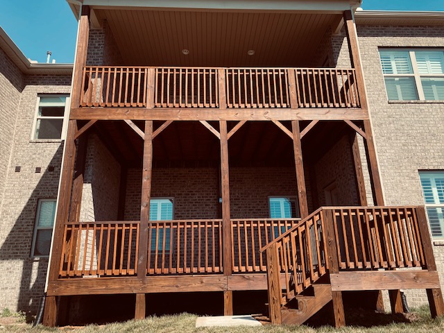 Three-level wooden deck attached to a brick building, with stairs leading up to the lower level, and railings on all levels.