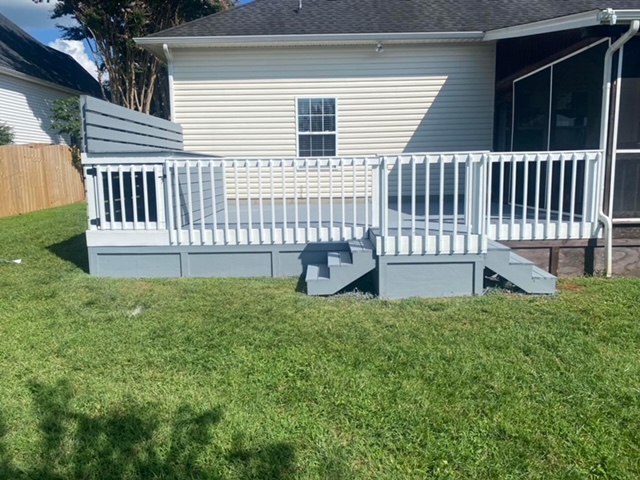 White wooden deck with railing attached to a house, with stairs leading down to a grassy yard.